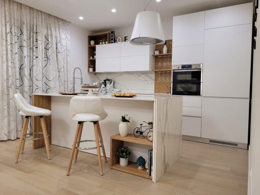 Cucina moderna con isola, sgabelli bianchi e armadi bianchi e in legno.