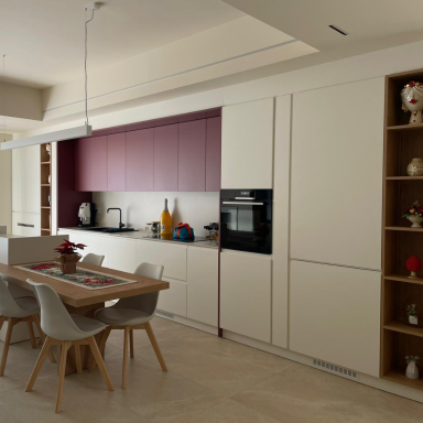 Cucina moderna con tavolo da pranzo, armadietti bianchi e parete bordeaux.